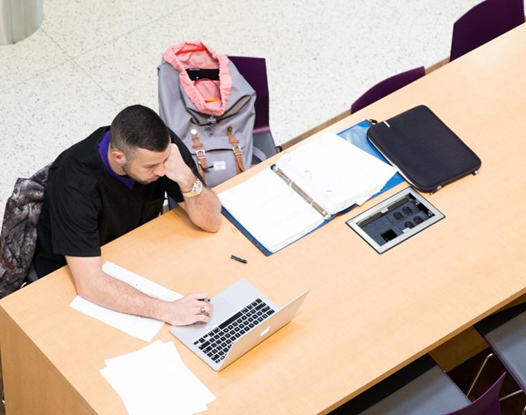Student studying with books and a laptop in the Bass Building