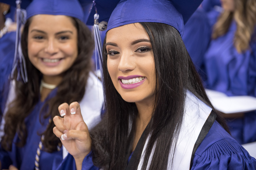 Happy graduate smiles while showing the frog sign